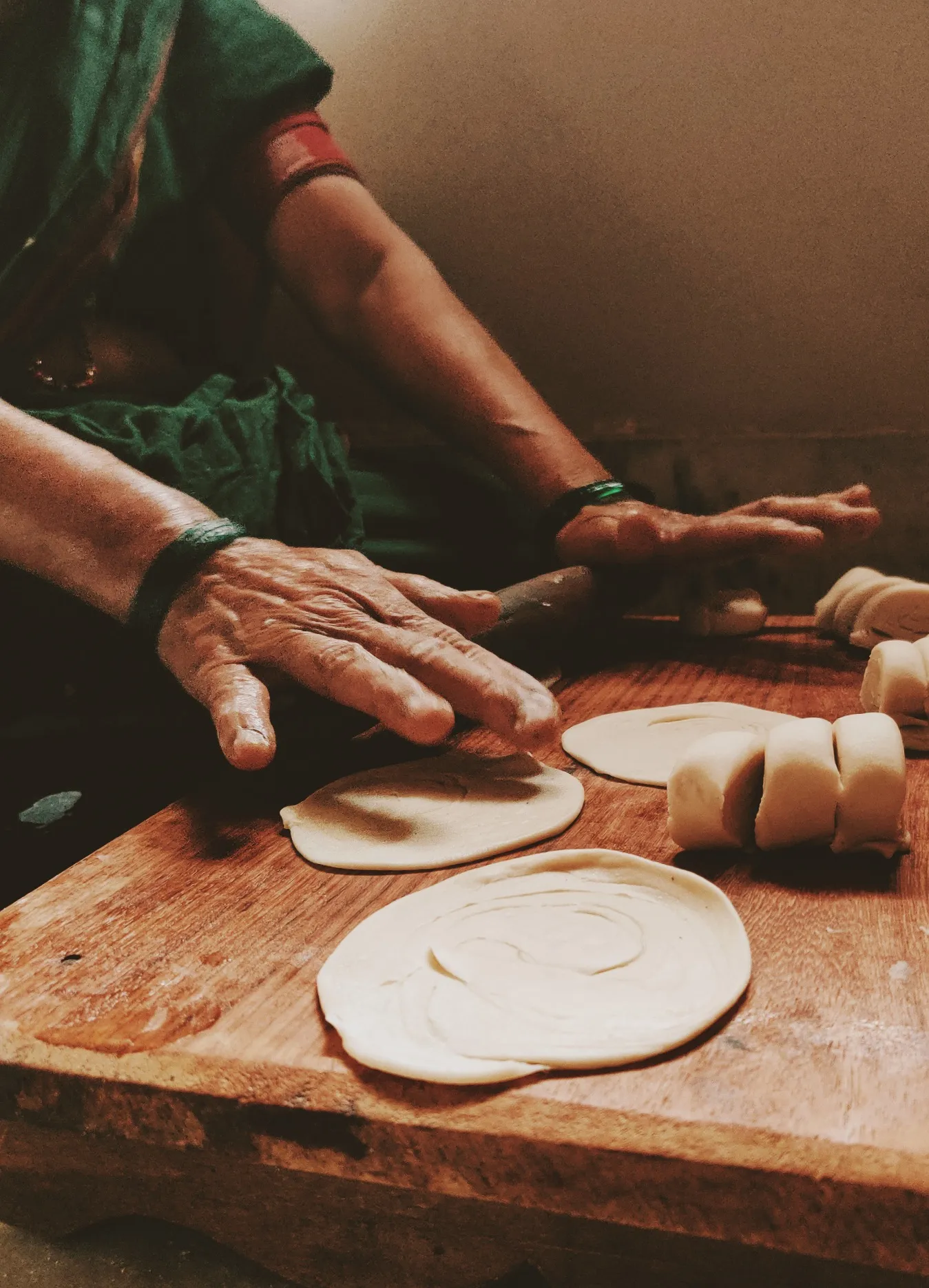 Hands rolling out flatbreads on a wooden board.