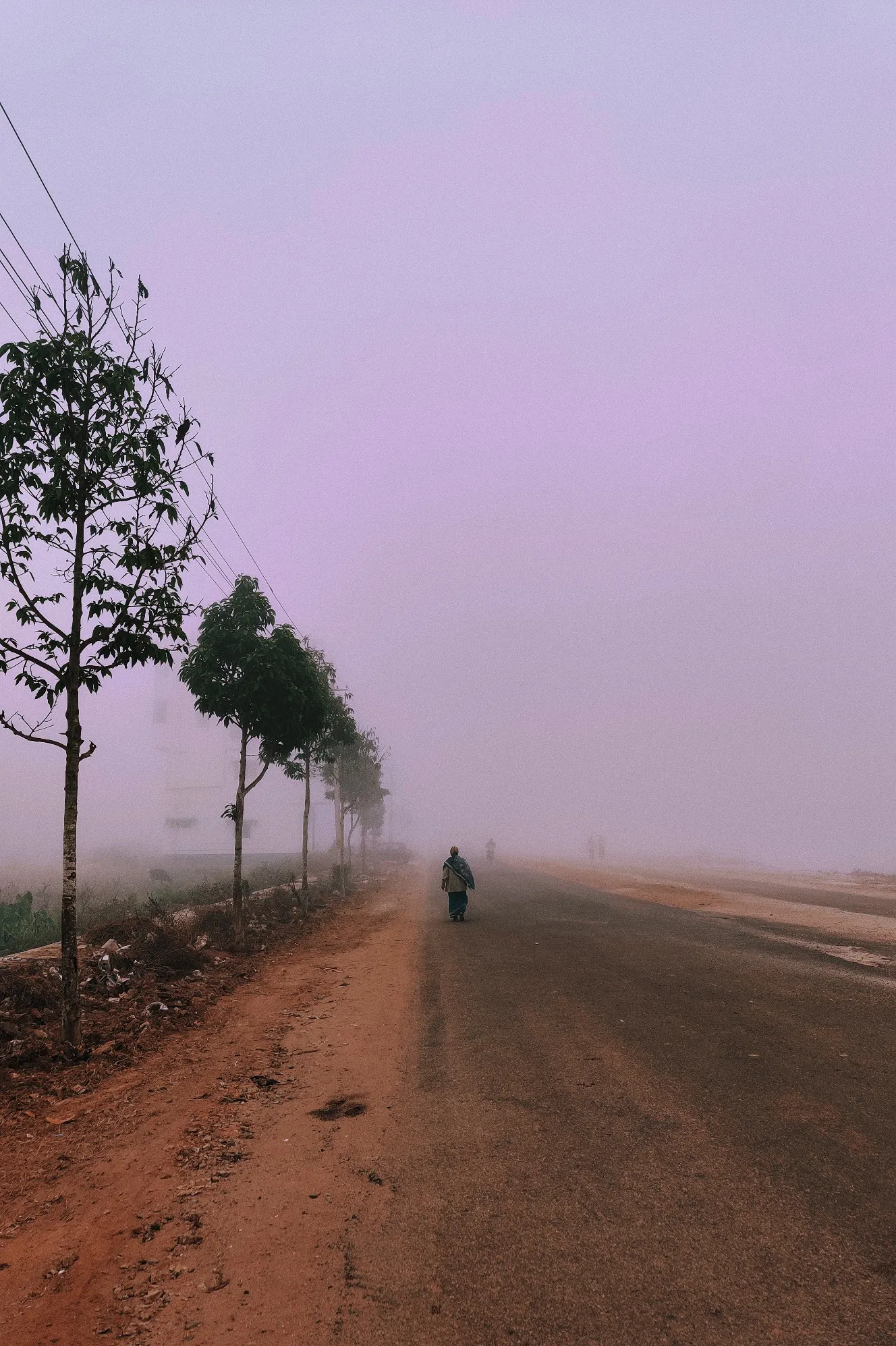 A dirt road disappearing into fog, one figure far down it.